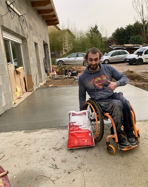 Benoit fayolle en fauteuil devant la terrasse en béton construite de ses mains grâce au don de ciment Vicat